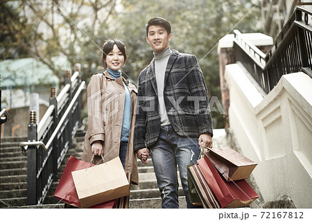 outdoor portrait of happy young asian couple standing on steps with paper shopping bags in hand 72167812