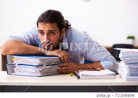 Young male employee unhappy with excessive work in the office 72168896