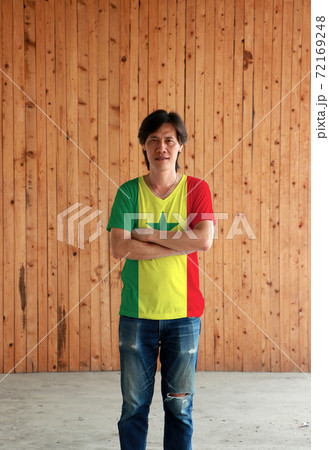 Man wearing Senegal flag color shirt and cross one's arm on wooden wall background. Man wearing Senegal flag color shirt and cross one's arm on wooden wall background. 72169248