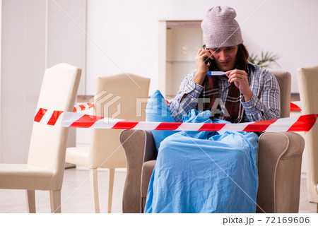 Young sick man measuring temperature at home during pandemic Young sick man measuring temperature at home during pandemic 72169606