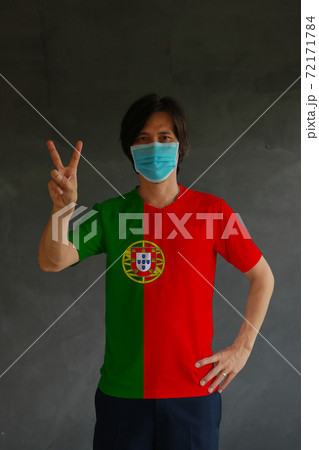 Man wearing hygienic mask and wearing Portuguese flag colored shirt and raising two fingers up Man wearing hygienic mask and wearing Portuguese flag colored shirt and raising two fingers up 72171784