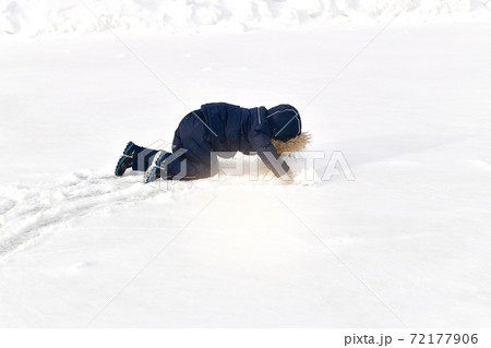 A child crawls on all fours in the snow in a winter jumpsuit with a fur hood. A child crawls on all fours in the snow in a winter jumpsuit with a fur hood. 72177906