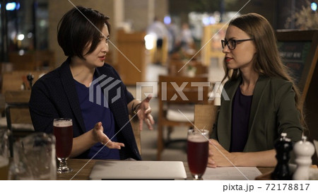 Two blonde and brunette women friends discussing plans sitting in a bar Two blonde and brunette women friends discussing plans sitting in a bar 72178817
