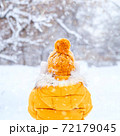 Back view of young woman wearing yellow jacket walks in snowy park 72179045