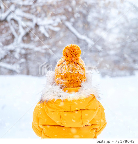 Back view of young woman wearing yellow jacket walks in snowy park 72179045