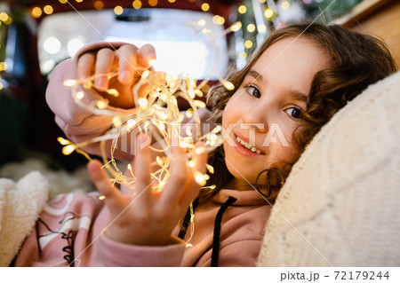 Little girl face with Christmas garland lights 72179244