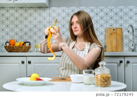 Young beautiful woman sitting at table and cleaning orange Young beautiful woman sitting at table and cleaning orange 72179245