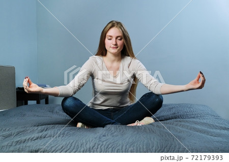 Relaxed young woman sitting at home in bed meditating girl practicing yoga Relaxed young woman sitting at home in bed meditating girl practicing yoga 72179393