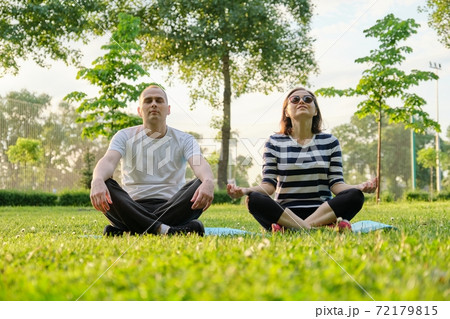 Couple, man and woman sitting in park on mat in lotus position and meditating Couple, man and woman sitting in park on mat in lotus position and meditating 72179815