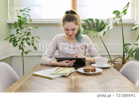 Teenager girl studying at home, student sitting at table using digital tablet Teenager girl studying at home, student sitting at table using digital tablet 72180041