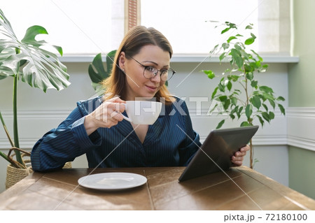 Smiling mature woman having breakfast at home reading digital tablet 72180100