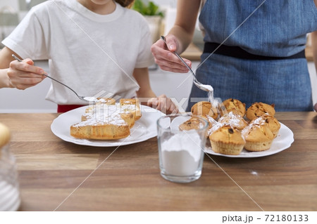 Kids sprinkling baked homemade muffins with white sugar powder 72180133