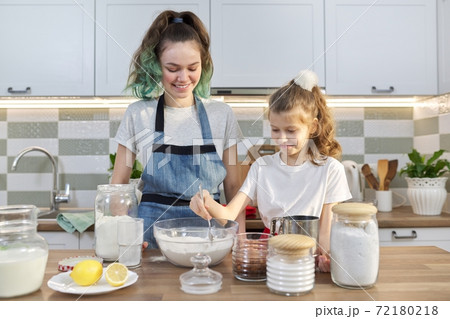 Two girls, teenager and younger sister, preparing cookies together in kitchen 72180218