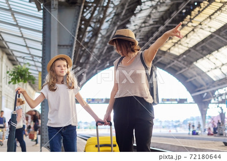 Happy mother and daughter child walking together at railway station with suitcase 72180644