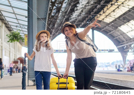 Happy mother and daughter child walking together at railway station with suitcase 72180645
