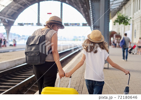 Happy mother and daughter child walking together at railway station with suitcase, back view 72180646