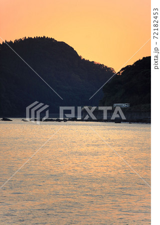 後ろに夕陽を被り油津港の海岸を走るキハ40 72182453