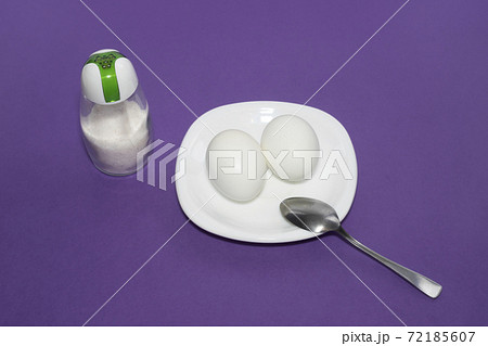 A dish of two eggs with a spoon and salt on a purple background. A dish of two eggs with a spoon and salt on a purple background. 72185607