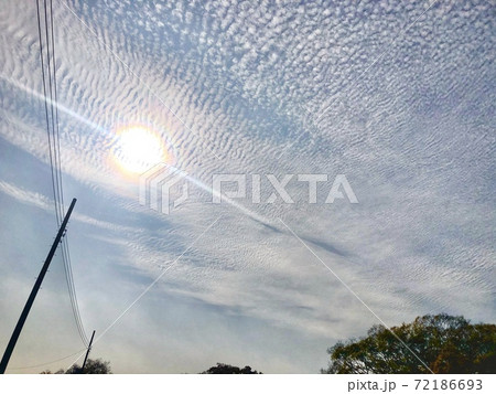 秋の鱗雲と輝く太陽がある空と連なる電線がある風景の写真素材