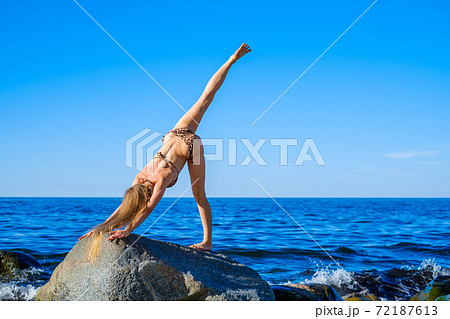 Slim female doing yoga against bright blue sky 72187613