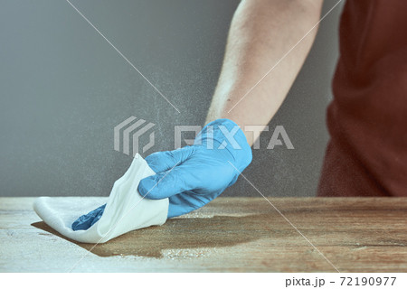A hand in a medical glove wipes the table. Grey background with splashes of disinfectant. A hand in a medical glove wipes the table. Grey background with splashes of disinfectant. 72190977