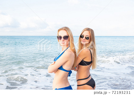 Portrait. Two attractive girls on the beach in bikini look at the camera through sunglasses, against the background of the sea Portrait. Two attractive girls on the beach in bikini look at the camera through sunglasses, against the background of the sea 72193231