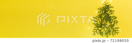 Christmas holiday banner. Xmas tree made from green arborvitae branches with luminous Xmas lights on yellow background. Alternative Xmas Tree. Xmas decoration from twigs. Happy New Year. Top view. 72198050
