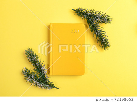 Xmas workspace. Yellow notepad-organizer on 2021 and two fir twigs on yellow. Planning for next year. Business greeting card. Top view. Minimal image. Copy space for text. 72198052