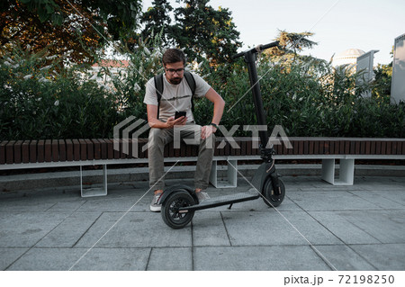 hipster man commuter with electric scooter outdoors in city, using smartphone. hipster man commuter with electric scooter outdoors in city, using smartphone. 72198250