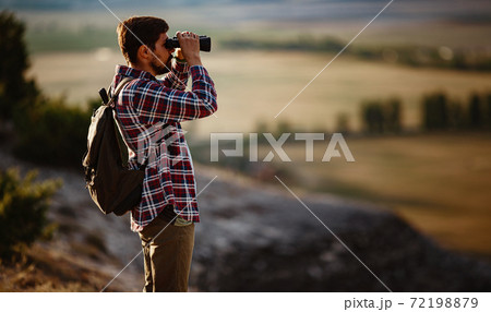Guy looking at binoculars in hill. man in t-shirt with backpack. 72198879