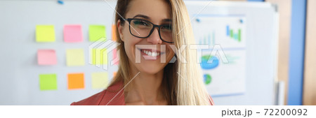 Smiling businesswoman stands in office behind on white board charts with business figures. Smiling businesswoman stands in office behind on white board charts with business figures. 72200092