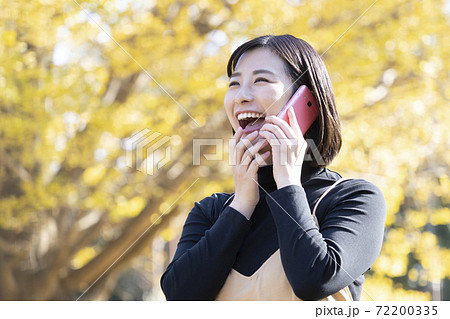 秋の公園で笑顔で電話する女性 72200335