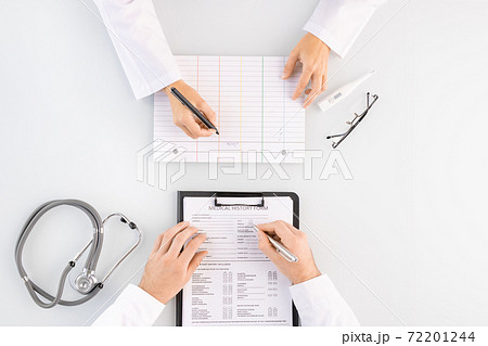 Overview of hands of male doctor filling in medical history form in clipboard 72201244