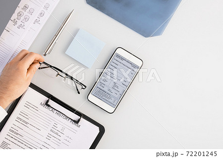 Flatlay of hand of doctor putting eyeglasses on table by medical history form 72201245