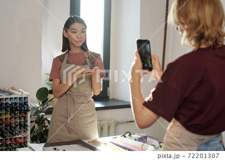 Young brunette woman with handmade glass bead on hand standing by workplace 72201307