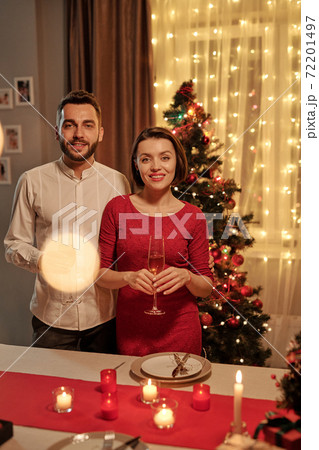 Happy couple with champagne standing by fesive table against Christmas tree Happy couple with champagne standing by fesive table against Christmas tree 72201497