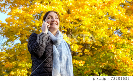 Brunette woman talking on the phone against the background of yellowed trees 72201635