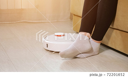 Woman in white socks lets robot cleaner pass sitting on sofa Woman in white socks lets robot cleaner pass sitting on sofa 72201652