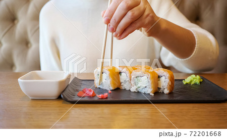Young unrecognizable woman eating rolls with salmon while sitting in a cafe 72201668