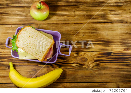 Lunch box with sandwiches, banana and apple on a wooden table. Top view, copy space 72202764