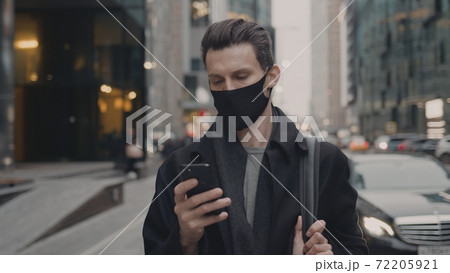 Man in protective mask with phone outside, city buildings and cars on background 72205921
