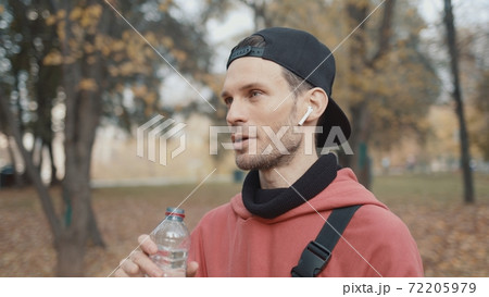 Man runner in red hoodie having a sips of water in city park, slow motion Man runner in red hoodie having a sips of water in city park, slow motion 72205979