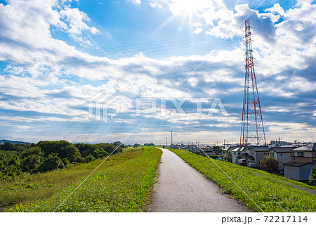 雲の切れ間から太陽の日差しが降り注ぐ広大な空と川沿いの道 72217114