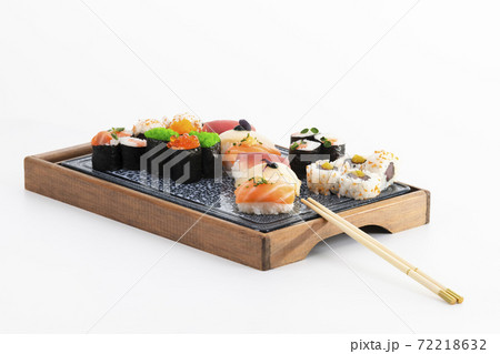 Close up of assorted maki, nigiri and uramaki with chopsticks on a wooden tray on a light background. Sushi and healthy food concept. Close up of assorted maki, nigiri and uramaki with chopsticks on a wooden tray on a light background. Sushi and healthy food concept. 72218632