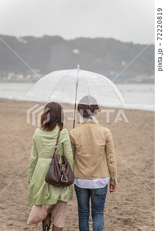 雨の海辺を傘をさしてデートするカップル 72220819