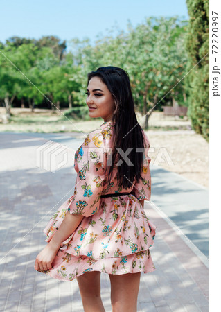 Beautiful brunette woman in a dress with flowers walks in the park in spring Beautiful brunette woman in a dress with flowers walks in the park in spring 72220997