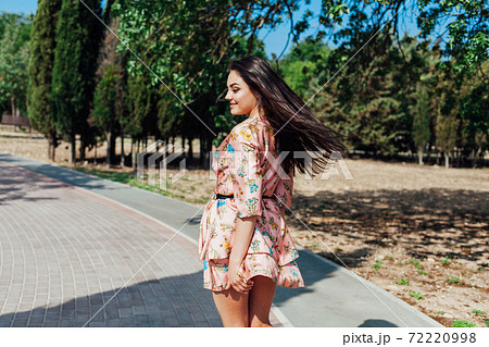 Beautiful brunette woman in a dress with flowers walks in the park in spring Beautiful brunette woman in a dress with flowers walks in the park in spring 72220998