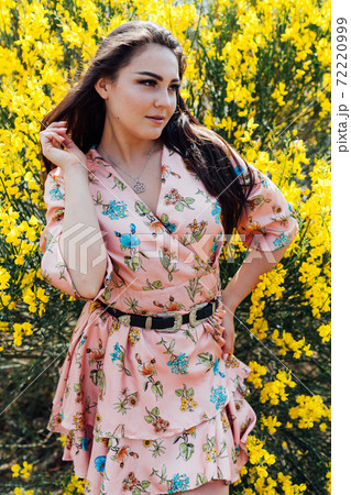 Beautiful brunette woman in a dress with flowers walks in the park in spring Beautiful brunette woman in a dress with flowers walks in the park in spring 72220999