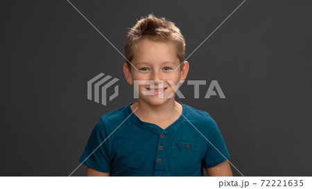 Cute schoolboy boy in dark blue t-shirt smiling at camera while standing in studio isolated on black background. Fashion concept 72221635