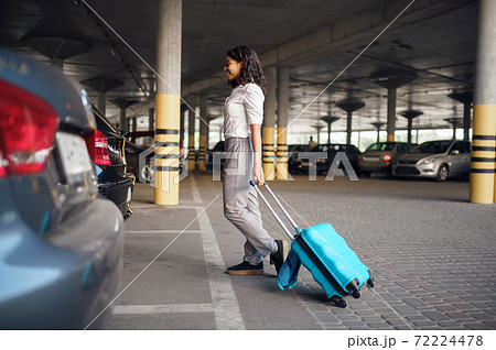 Young woman with suitcase in car parking 72224478